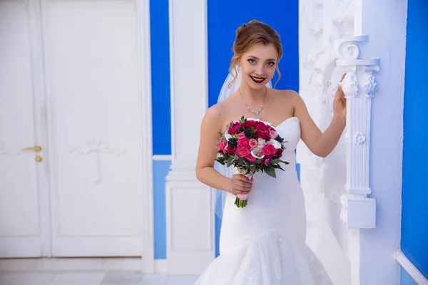 Posiert die Braut in einem Saal mit blauen Wänden und weißen Gipssäulen. Sie ist überrascht von der Schönheit des Interieurs und berührt die Statue. das Mädchen lächelt nicht nur mit den Lippen, sondern auch mit ihrem — Stockfoto