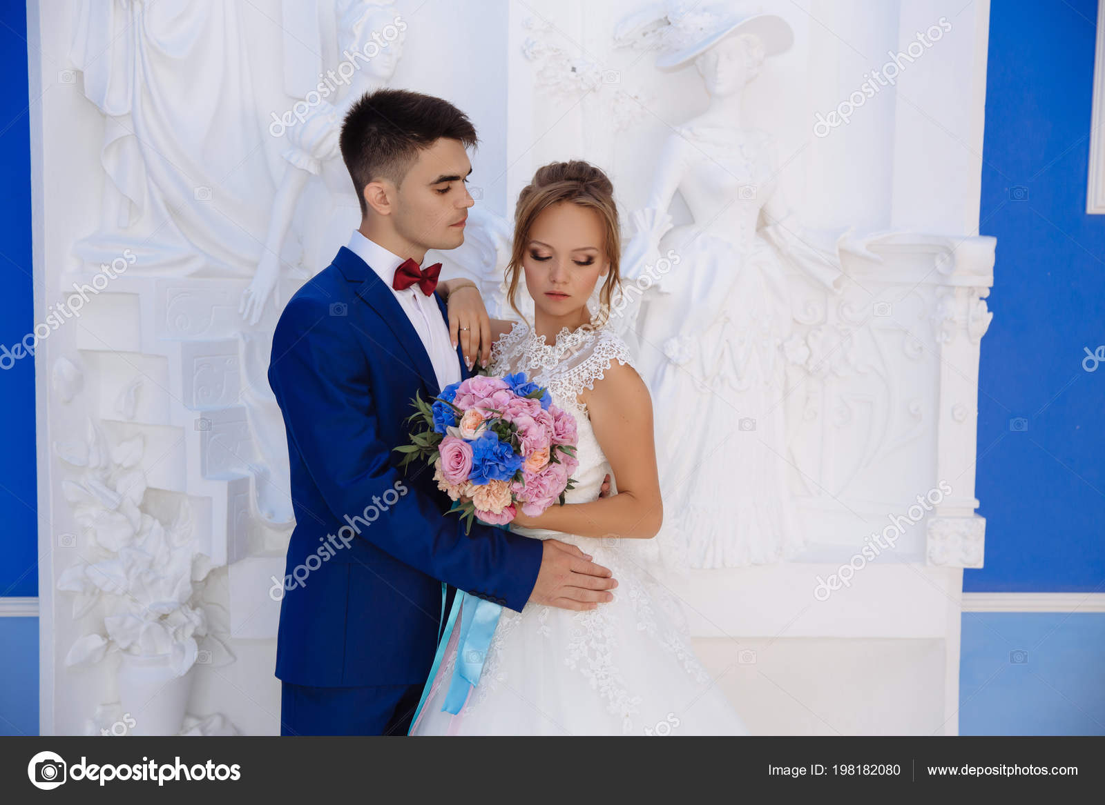 The Bride And Groom Posing Against A White Sculptural Wall