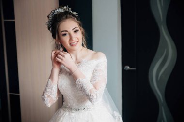 Dantelli beyaz elbise ve duvak gelin törene gidiyor. Küpe üzerinde koyarak ve gülümseyen bir kız portresi.