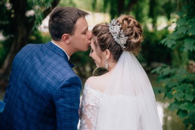 Arkadan Görünüş bir adam yavaşça gelini alnından öper. Yeni evliler Close-up yürüme park, birbirlerine zevk. Gelin saçında şık dekorasyon ile.