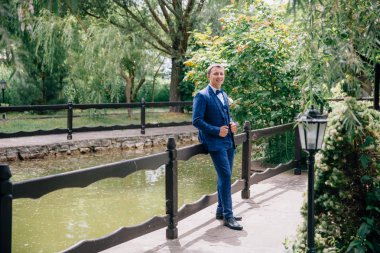 Bir düğün için hazır ve düzgün giyimli adam. O parkta elini kolunu sallaya dönüyor, gölette görünüyor ve gelecekteki eşi için bekler.