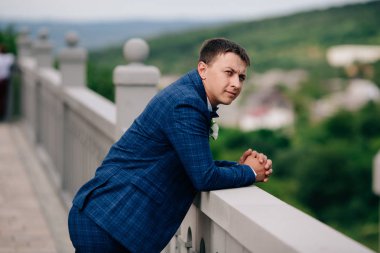 İş adamı dirseklerini parapetin üzerinde kendi işlerini hakkında fazla düşünüp eğildi. Adam ikindilerde alnına yalnız soruyorlar. Damat düğüne gitmeye karar verir ya da değil.