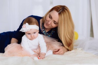 Yakın çekim bir bebek provati üzerinde oturur ve bacağını dokunmadan yoğunlaşmaktadır. Annesi arkadan oturur ve onu, gülümseyerek ve bakan saatler.