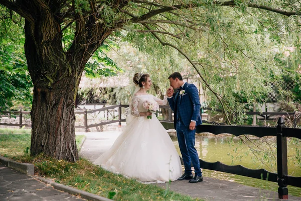 Mannen tittar uppmärksamt på kvinnan och kysser hennes hand ömt. En kvinna i en bröllopsklänning och en bukett blommor ler försiktigt mot sin älskade. Paret fick bara gifta. — Stockfoto