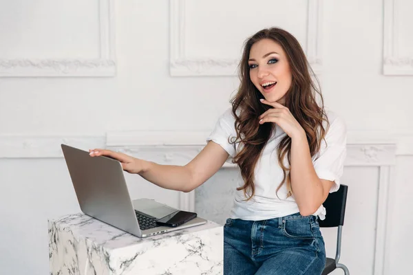 Eine hübsche Studentin mit welligen dunklen Haaren trägt ein weißes Oberteil und stylische Jeans, schreibt gerade einen Artikel, schließt ihren Laptop und lächelt fröhlich. — Stockfoto