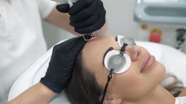 Doktor güzellik uzmanı bir sabahlık ve eldiven bayan hasta, yüzünde lazer yordamları gerçekleştiren yakın çekim. Plastik ve ectatic cerrahi, klinikte cilt soyma cilt. Tıbbi