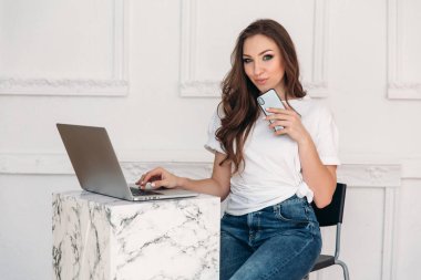 Tatlı bir şık güzel Avrupa kız onun laptop, o does onun en sevdiği şey, bir smartphone bir arkadaş için bir kısa mesaj yazmak için onun elinde tutan mutlu bir restoranda oynuyor.