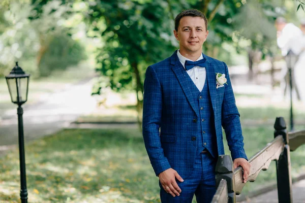 Portrait of a man in a chic suit. The guy is going to get married today, hes wearing a blue suit, a bow-tie and a little worried before the wedding ceremony begins.