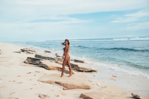 对白色沙漠海滩和蓝色水的模型的侧面视图。一个苗条, 被晒黑的女孩沿着白色的沙子穿着时髦的性感泳装散步. — 图库照片