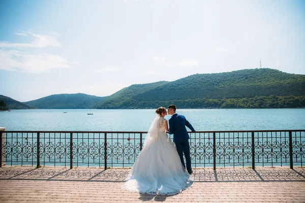 Gli amanti si baciano sullo sfondo delle montagne e del lago blu. Giorno di nozze in un posto pittoresco stupefacente . — Foto Stock
