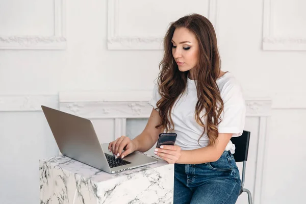 Ein schönes europäisches weibliches Model, das an modernen Geräten arbeitet, in einem Café sitzt, ein Mädchen in lässiger Kleidung und sehr enthusiastisch an einem Laptop arbeitet. — Stockfoto