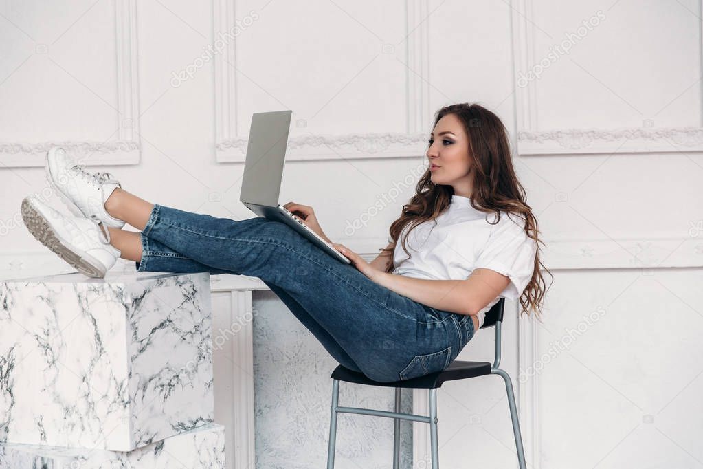 An attractive freelancer girl works in an apartment, sitting comfortably on a chair, throwing her feet on a table and putting her laptop on her lap.