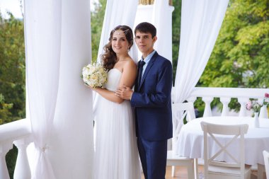 Terasta, adam yavaşça poz yeni evli genç evli bir çift tarafından omuz karısı hugs.
