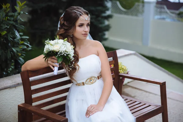 Retrato de una hermosa novia joven en una boda de estilo griego, posando sentado en un parque verde . — Foto de Stock