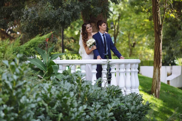 Um casal amoroso caminha no jardim após a cerimônia de casamento. A noiva e o noivo se abraçam e se divertem. a menina abraça seu homem por trás, e sorri feliz . — Fotografia de Stock