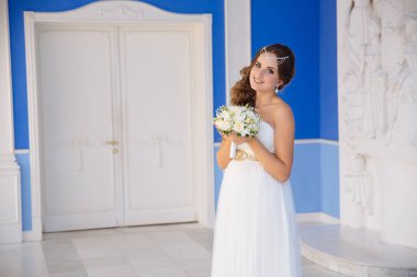 Bir buket çiçek mavi duvarlı bir salonda poz ile beyaz elbiseli güzel genç neses.