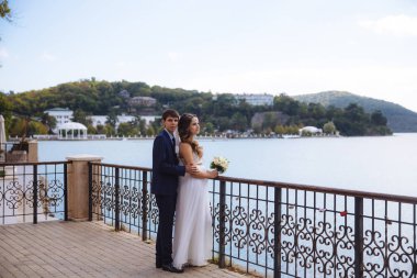 Bir kız bir gelinlik bir buket çiçek ile onun elinde bir buket çiçek ile dock üzerinde duruyor ve nehir su yüzeyine görünüyor. Onun arkasında da damat kucaklayan bir