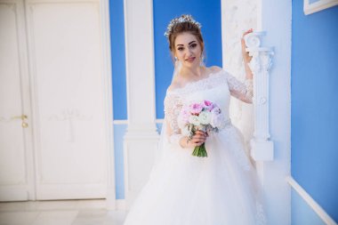 Gelin gülümsüyor ve sütunlarla, büyük salon yürür inceler ve dokunur. Gelinler bir buket pembe çiçek eldir.