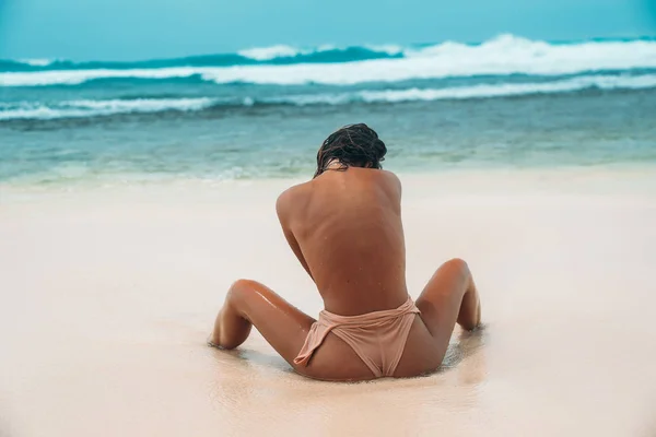リア オーシャン ビーチでベージュの水着を着ているスポーティな女の子のセクシーなお尻を表示。女性の体、裸の背中と肩の部分。ブラなしビキニの若いモデルの日焼けブーティ. — ストック写真