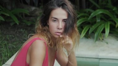 Güzel manken delici bir cinsel bakışla saçları tropikal çalılar ve ağaçlar çerçevede bir kamera poz ile oynarken yavaş hareket fotoğrafını Close-up