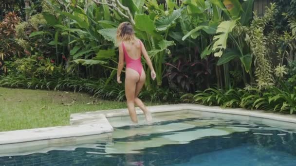 Lentamente atirando steadikam sexy modelo esbelto esportes em um maiô vermelho emerge da piscina, vira as costas, mostra uma bunda suculenta, tem pernas retas longas e uma cintura fina . — Vídeo de Stock