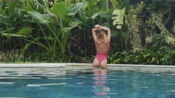 Close-up slow-motion shot steadicam view from pool young girl in bright swimsuit with beautiful round ass pulling her arms up, enjoying her trip to paradise tropical place. — Stock Video