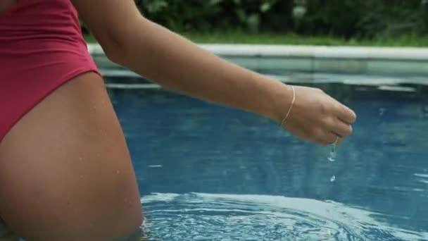 La mano gentile di una giovane ragazza attinge acqua dalla piscina, le gocce lentamente svuotano le dita. Modello con un giro sexy culo posa in piscina, close-up rallentatore tiro, steadicam . — Video Stock