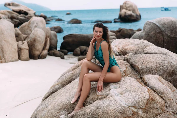 Uma jovem sexy e bonita de pele escura senta-se em uma pedra, em uma praia deserta branca, desfrutando do fluxo de vento que desenvolve seu longo cabelo escuro, fechou os olhos com prazer. . — Fotografia de Stock