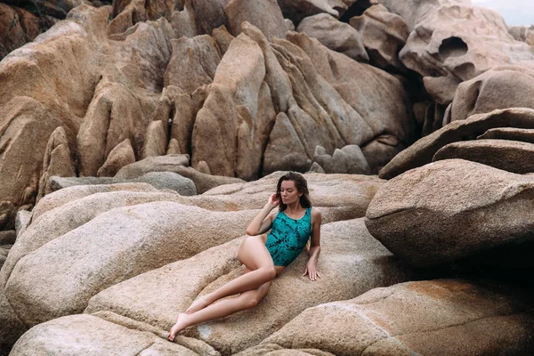 Sexy junge schöne Mädchen in einem Badeanzug, die sich auf einem einsamen felsigen Strand allein ausruhen. das Mädchen liegt und sonnt sich umgeben von Felsen und Felsen, genießt ihre Einsamkeit und die Schönheit der Natur. — Stockfoto