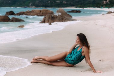 Yalnız güzel bir genç kız büyük kayalık taşlarla beyaz plaj kıyısında yatıyor, deniz sörf hayran, düşünceli horizon adlı görünüyor.