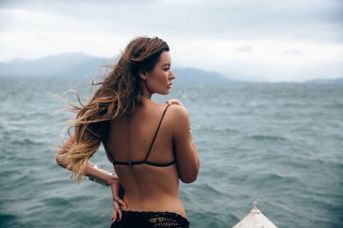 Uzun kalın saç, görünümü ile bir şaşı tarafa, güzel bir genç Avrupa kadınla profil arka görünümünden portre siyah beach kılığına girmiş bir ince bel üzerinde elini tutar.