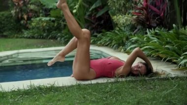 Uzun düz ayak bir ince, güzel genç kız küçük bas özel bir villada zemin karşı yatıyor ve ayakları havada tekmeler, dudağını ısırıp, parmağına saç bir iplikçik katlanmış