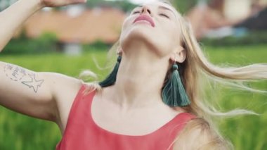 Gri gözleri olan genç bir sarışın kız bir yakın çekim yavaş hareket resmi doğa yürüyüşleri, nazik onun dans sahiptir, kamera ve gökyüzü görünüyor, temiz yüzünü elleriyle dokunuyor.