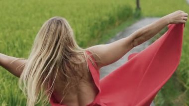 Bir hafif makyaj ve gevşek dağınık sarı saçlı güzel kız çevresinde doğa, kırmızı eteği bir elinde tutan fırtınası genç bir close-up kumaş rüzgar, ikinci el uzanır.