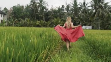 Uzun ipek bir elbise, ishal uzakta birisi, uzun bacaklar ile güzel kız giyer hareket halinde çekim arka görünümünden bir pirinç alan palmiye orman üzerinde off-road, ishal, uzun eteği ile her ikisi tutar