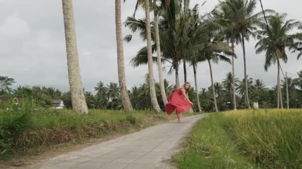 Visão inferior, tiro em câmera lenta, a menina em um vestido longo brilhante vai em meias sob as palmas das mãos, caminha e admira os terraços de arroz, começa a correr rapidamente. Uma jovem atlética em um feminil — Vídeo de Stock