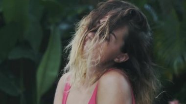 Güzel seksi manken kısa kıvırcık saçlı tropikal ormanda saçları ile oynarken rahatlatıcı sahiptir, bir kahverengi toka, boyalı saç.
