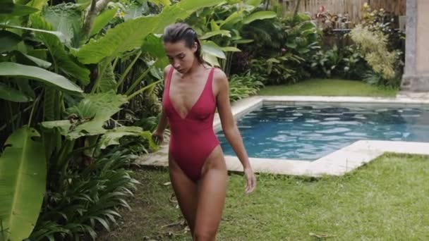 A sexy young slender athletic girl in a berry swimsuit emerged from the pool, her breasts tightly clings clothes, dark and wet hair, she follows her warm towel, slowed down shooting to the steadicam — Stock Video