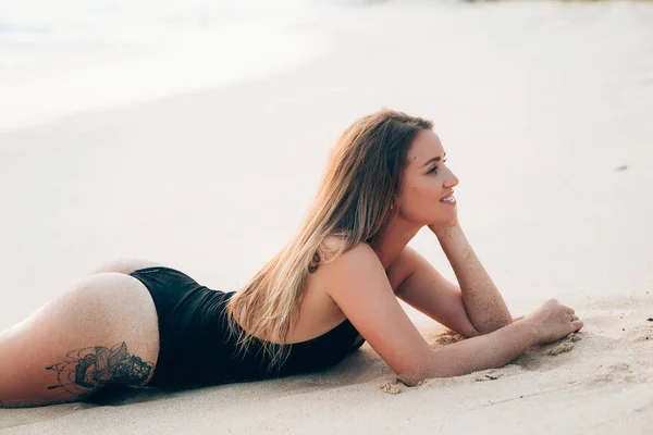 Uma jovem europeia com cabelos longos e lisos fica na praia, veste um fato de banho preto elegante e caro, comunica com seus amigos, ri e se diverte nas férias. . — Fotografia de Stock