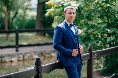 Bir adam bir ahşap oyma çit poz. Şık kıyafet, beyaz gömlek ve yaka çiçeği düğün töreni için ihtiyaç vardır. Damat parkta yürüyüş ve gelin için bekliyor.