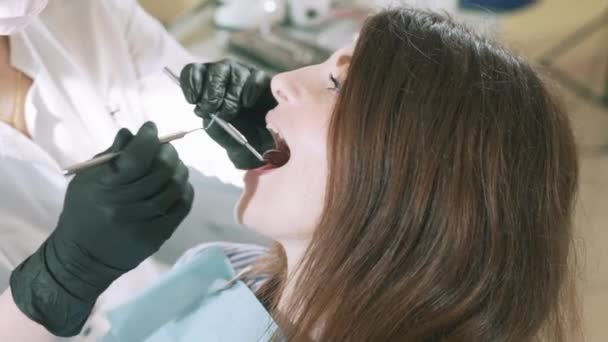 Detail oříznutého snímku zpomalený záběr mladá dívka přišla na rutinní vyšetření k zubnímu lékaři. Specialista s pomocí zubní zrcátko a stěrky podvádí zuby pacientů — Stock video