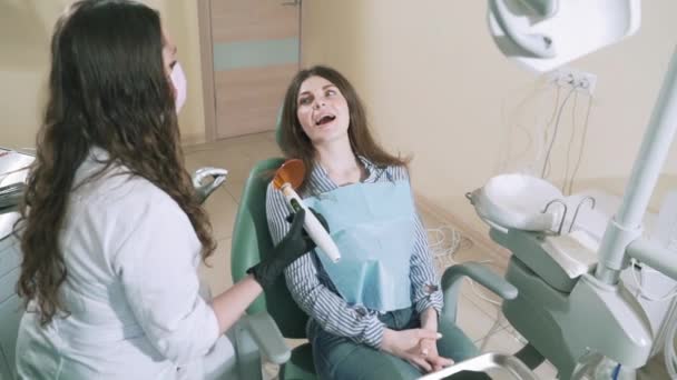 Bromsat upp skytte flicka liggande i stolen, leende. Kvinna läkare ska borra sin värkande tanden med en modern trådlös borr. På gott humör i tandläkarens — Stockvideo