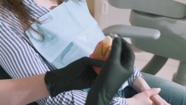 Primo piano rallentatore girato donna stazionaria dentista tiene in mano un modello di denti umani, mostra la sua paziente la tecnologia di installazione di protesi. Il concetto di odontoiatria, dentiere, sorriso, odontoiatria — Video Stock