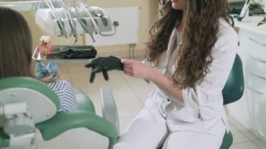 Yakın çekim ağır çekim çekim steadikam Doktor dişçi hastalar diş incelemek hazırlanıyor, elindeki steril Medikal Ürünler koyar. Kız bir koltuk dişçi ofisinde oturuyor.