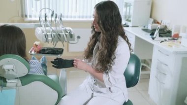Uzun siyah kıvırcık saçlı bir kadın dişçi hastalar ofisinde alır. Doktor diş sağlık muayenesi için hazırlar, steril Medikal Ürünler ellerinde, yavaş hareket steadicam için çekim koyar