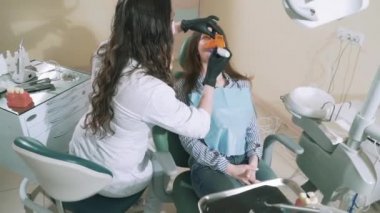 Yavaş yavaş çekim dişçi ofisinde genç kız hastaya bir mühür koymak ve ona bir photopolymerizer ile ısıtıyor. Diş tedavisi, mühürler, matkap, insanlar, sağlık, güzellik kavramı