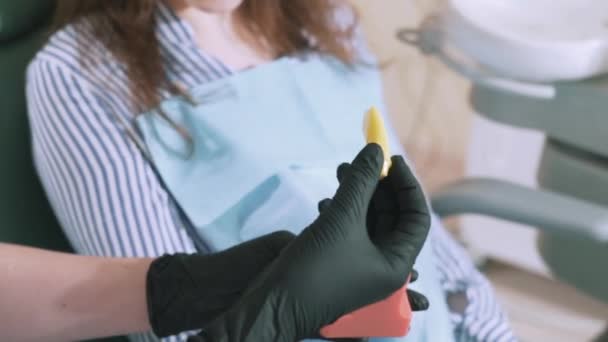 O dentista em seu consultório leva o paciente, mostra-lhe a estrutura dentária no modelo artificial, tira a dentina, mostra como ela se parece. Close-up tiro em câmera lenta steadikam — Vídeo de Stock