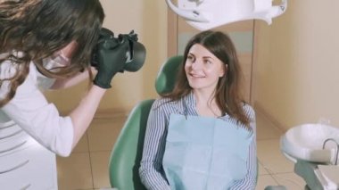 Geniş kameraya gülümseyen bir diş sandalye çekici parlak kız. Bir kukla işini tabanına eklemek için bir diş hekimi tarafından fotoğraflandı. Ağır çekim. Kavram sağlıklı ve güzel dişler, gülümse