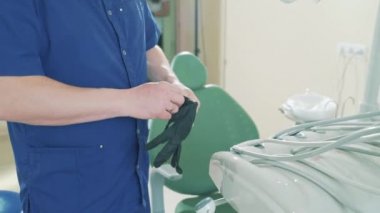 Bir yavaş hareket atış bir adamın kolunda diş ofiste ayakta Medikal eldiven koyarak tıbbi bir elbise içinde kırpılmış bir çerçeve Close-up doktor hasta almaya hazırlanıyor