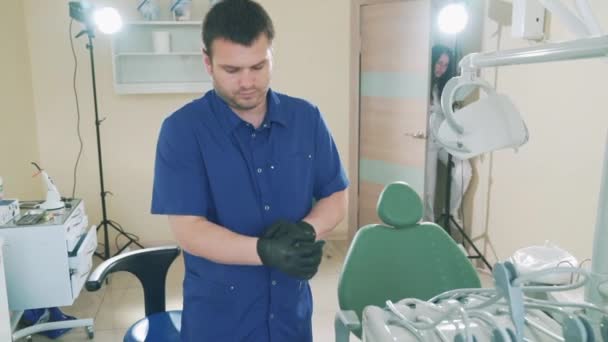 Tomando lentamente fotos de los médicos jóvenes retratos de un hombre en su consultorio dental se prepara para recibir a un paciente, se pone guantes médicos en las manos, un cliente entra en la habitación . — Vídeos de Stock